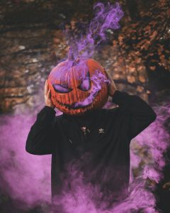 a man with a Jack-O-Lantern on his head, surrounded by purple smoke