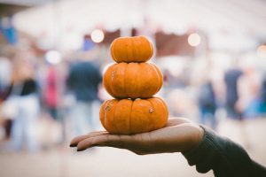 a woman’s outstretched hand holding three mini pumpkins that are stacked up