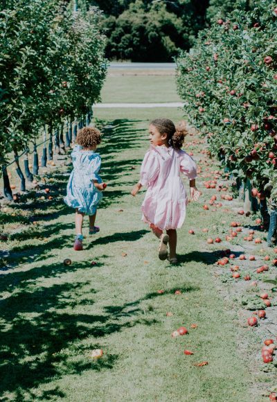 two girls running down the aisle of an apple orchard