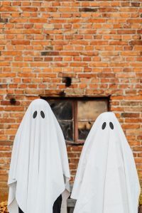 two kids wearing sheets as ghost costumes in front of a brick wall