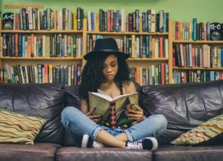 a teen girl sitting on a couch in a library, reading a book