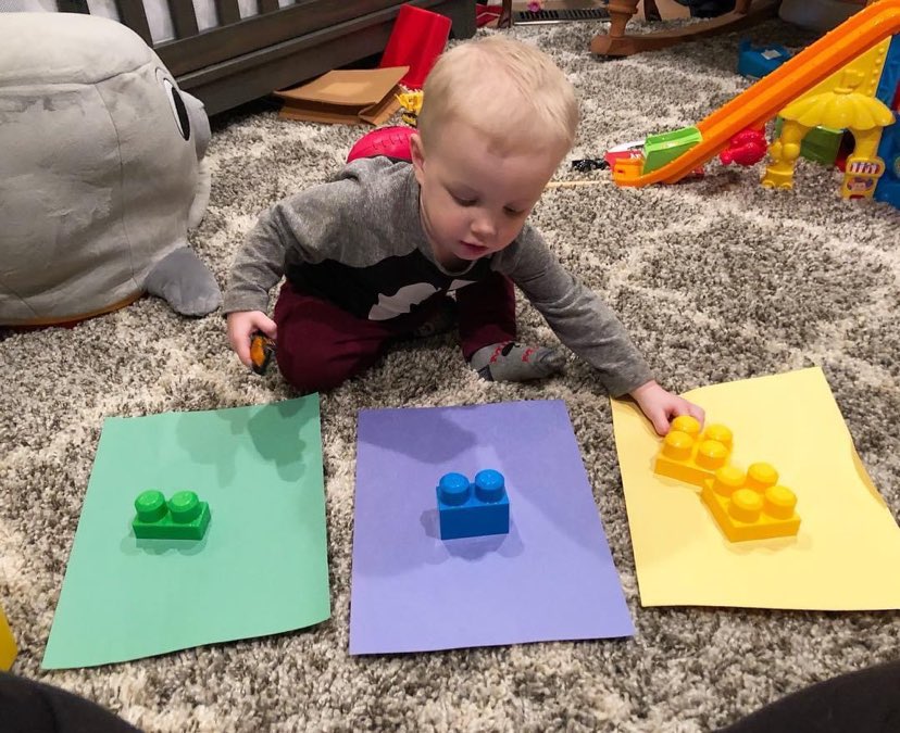 a toddler color-matching Duplo blocks onto colored paper as a STEM activity