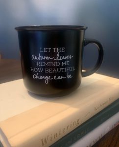 a black coffee mug with the words, “Let the autumn leaves remind me how beautiful change can be.” written in white