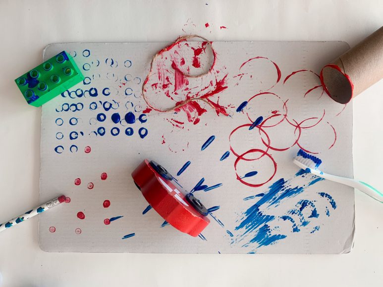 a piece of paper painted by using legos, toilet paper tubes, and other materials in place of brushes