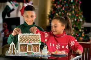 a brother and sister decorating a gingerbread house together as a holiday tradition