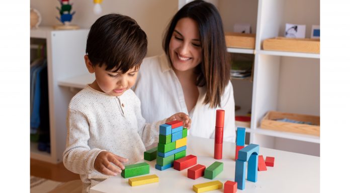 a teacher sitting with a child, encouraging him as he builds with blocks