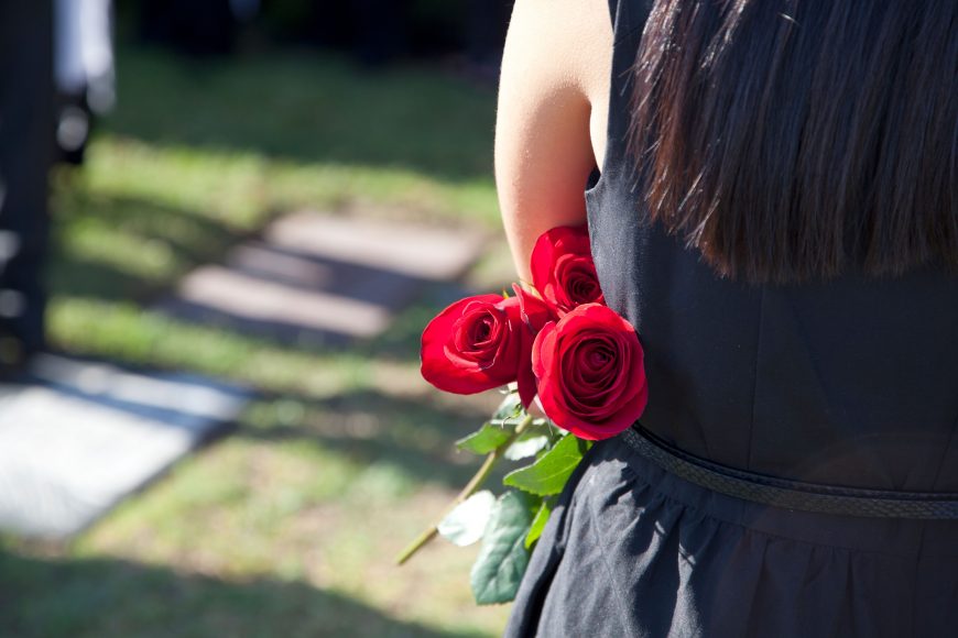 a woman from behind holding roses at a cemetery as she deals with death and grieving