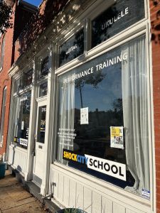 A brick building with a sign in the front window for Shock City School in Maplewood, MO