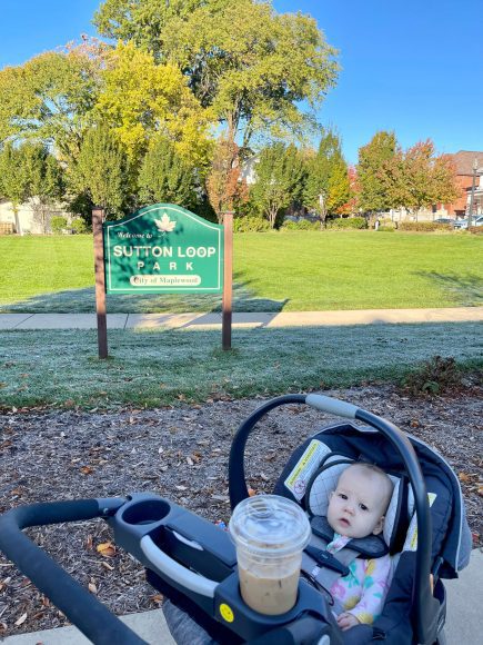 a stroller with a coffee in the cupholder and a baby in the seat in front of a Sutton Park sign in Maplewood, MO