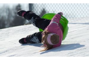 a girl tipping sideways off of her sled in the snow
