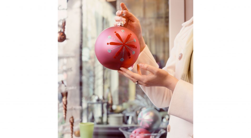 a woman holding a large red Christmas ornament in a holiday boutique