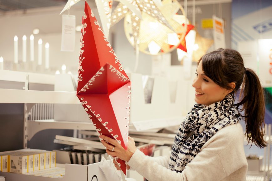 a woman in a white coat holding up a large red holiday star ornament in a shop