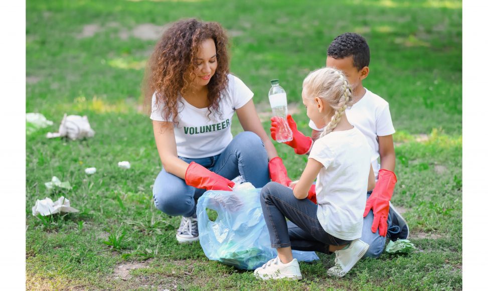 a woman volunteering with two kids to clean up trash in a park