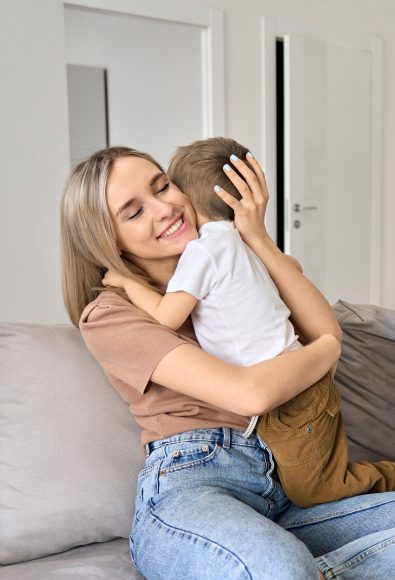 a mom sitting on the couch as she gets a hug from her toddler son