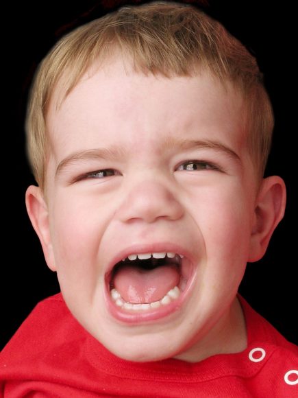 a close up of a little boy in a red shirt crying with his mouth wide open