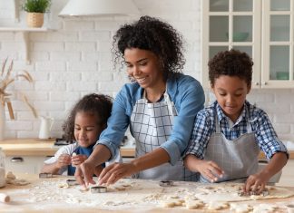 an African American mom rolling out dough with her apron-clad son and daughter