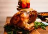 a cooked turkey on a wooden table with side dishes in the background for Turkey Day