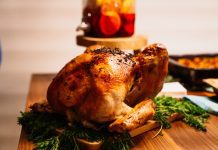 a cooked turkey on a wooden table with side dishes in the background for Turkey Day