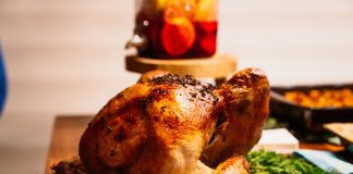 a cooked turkey on a wooden table with side dishes in the background for Turkey Day