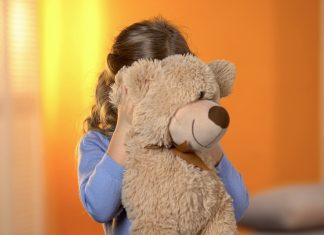 a shy girl hiding behind her teddy bear