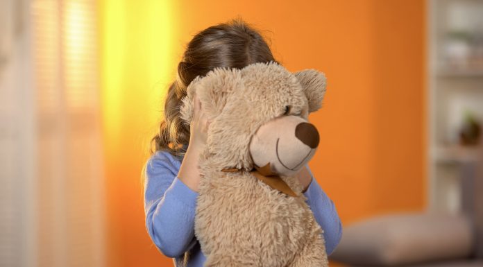 a shy girl hiding behind her teddy bear