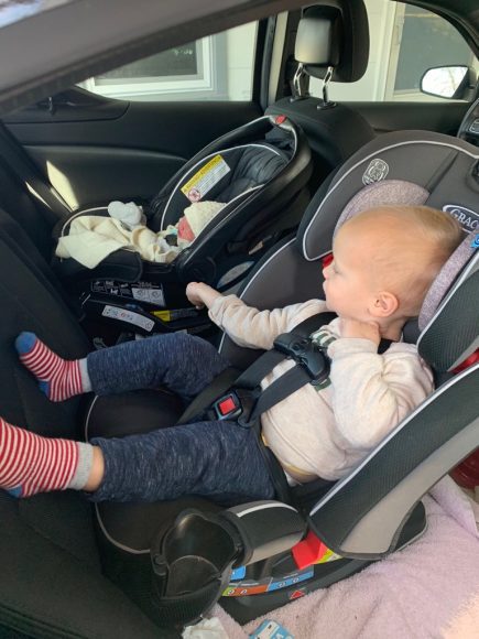 a toddler boy and his newborn sister, buckled into carseats in the backseat of their car