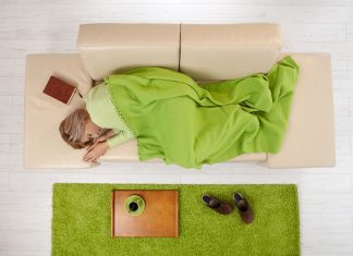 a woman napping on a cream colored couch, with a line green blanket pulled up over her