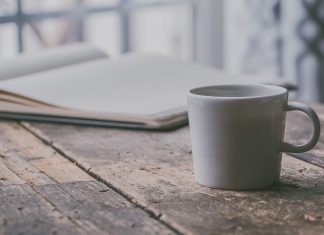 a simple white mug on a wooden table next to an open journal