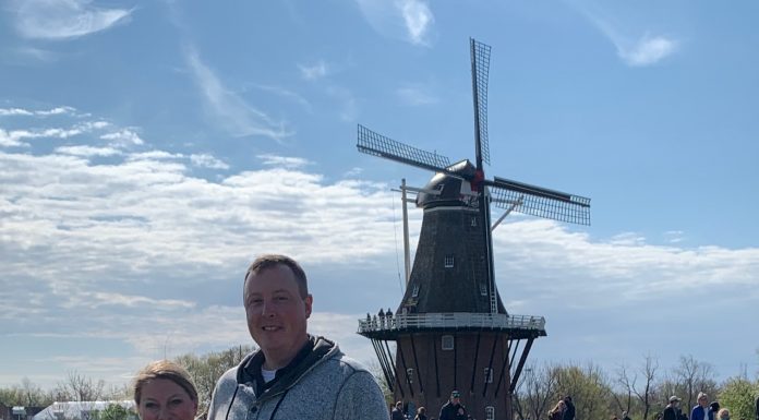 a husband and wife standing in front of a windmill in a field of tulips while on a trip to Holland, Michigan