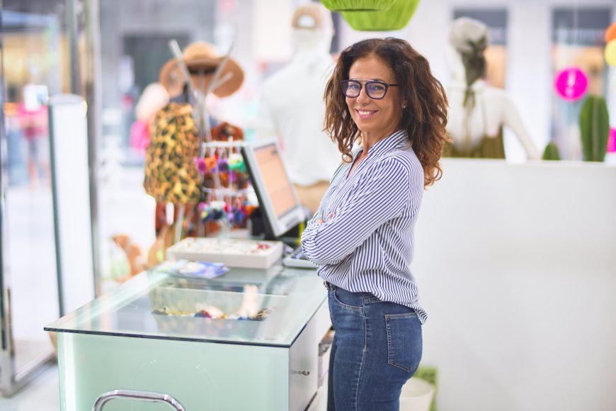 Middle age beautiful clothes shop owner woman smiling happy and confident waiting customers at counter