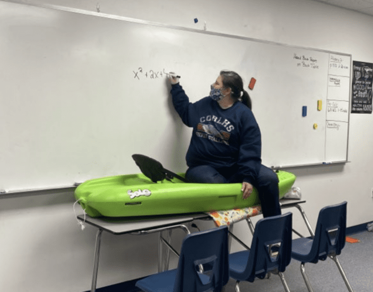a teacher sitting in a kayak as she writes a math problem on the white board