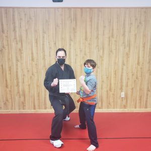 a boy and his karate instructor posing with an orange belt and a certificate