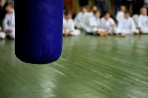 a kickboxing bag in the foreground and a blurred out karate class of kids in the background