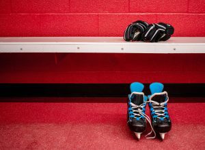 a pair of hockey skates on the ground and a pair of hockey gloves on the bench in a locker room with a red painted wall
