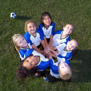 a team of young girls huddling together on the soccer field