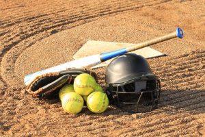 softballs, a softball bat, and a helmet on the ground near home plate
