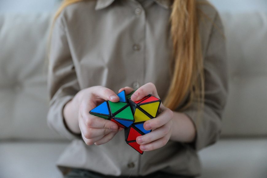 a girl on a couch working with a Rubik’s cube type fidget toy, symbolizing giftedness and perfectionism