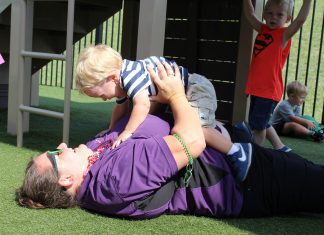 a preschool teacher laying on the grass as she picks up a preschool child at Kiddie Academy in O’Fallon, Missouri