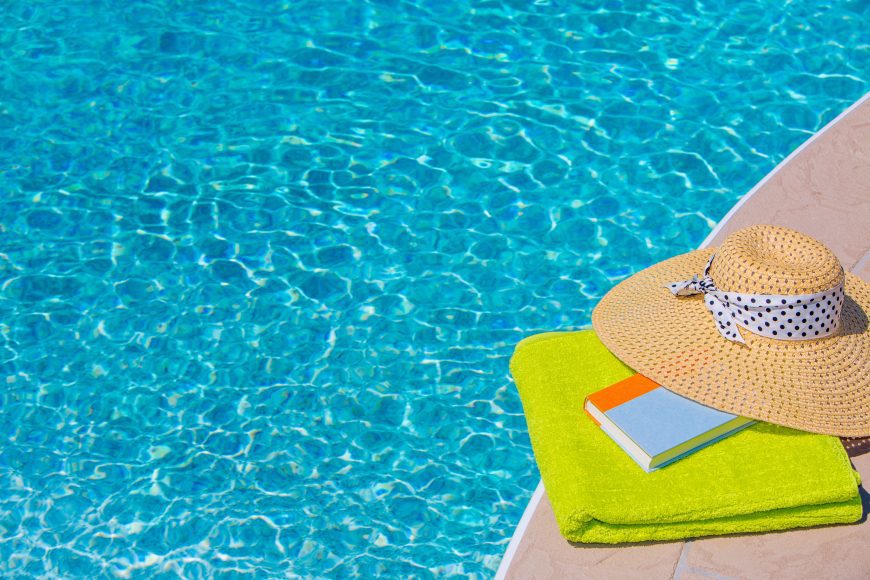 a lime green towel folded and laid by the edge of a pool with a book and sunhat on top of it