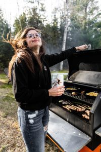 a woman standing in front of the grill, grilling burgers and hot dogs