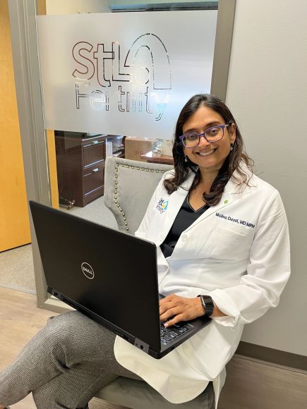a doctor sitting with her laptop in front of the logo for STL Fertility in St. Louis