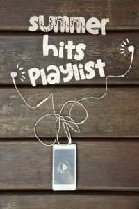 an iPod with ear buds on a wooden table with the words, “Summer Hits Playlist” written above