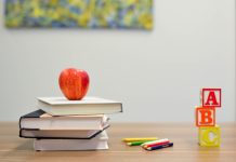 a stack of books with an apple on top that sits on a desk next to colored pencils and A, B, C blocks to represent back-to-school