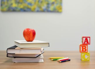 a stack of books with an apple on top that sits on a desk next to colored pencils and A, B, C blocks to represent back-to-school