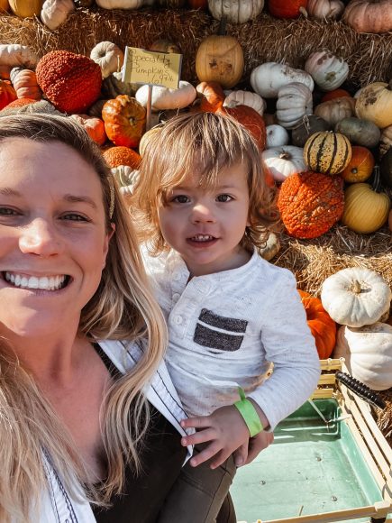 a mom holding her toddler son at a pumpkin patch