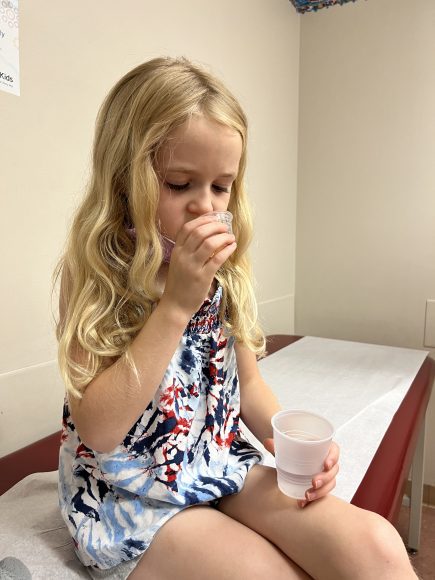 a little girl taking a sip of medicine at the doctor’s office