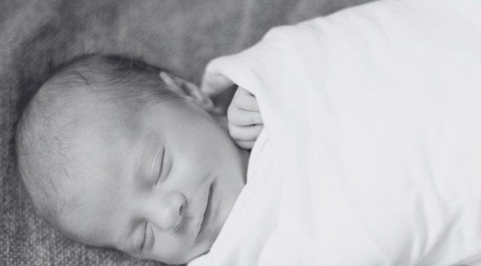 a black and white photo of a newborn baby swaddled up and sleeping with a smile on his face