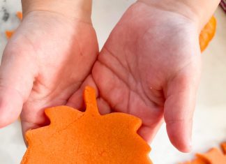 a child holding an orange leaf cut from play dough with the cookie cutter and scraps in the background