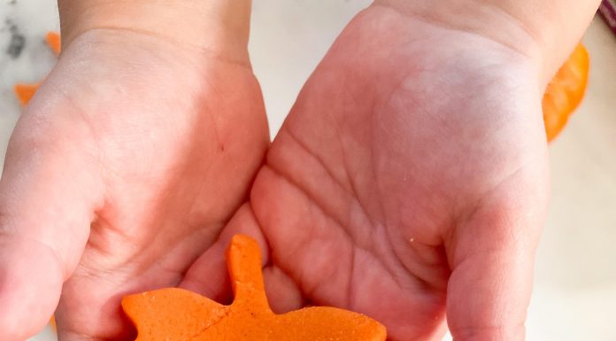 a child holding an orange leaf cut from play dough with the cookie cutter and scraps in the background