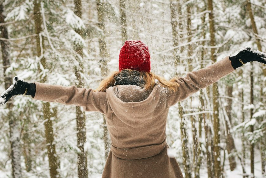 a woman standing with her arms outstretched in the woods as it is snowing